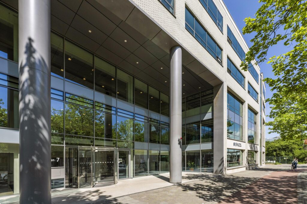 Modern office building with large glass windows and "Spaces" entrance on Mr. Treublaan in Amsterdam.